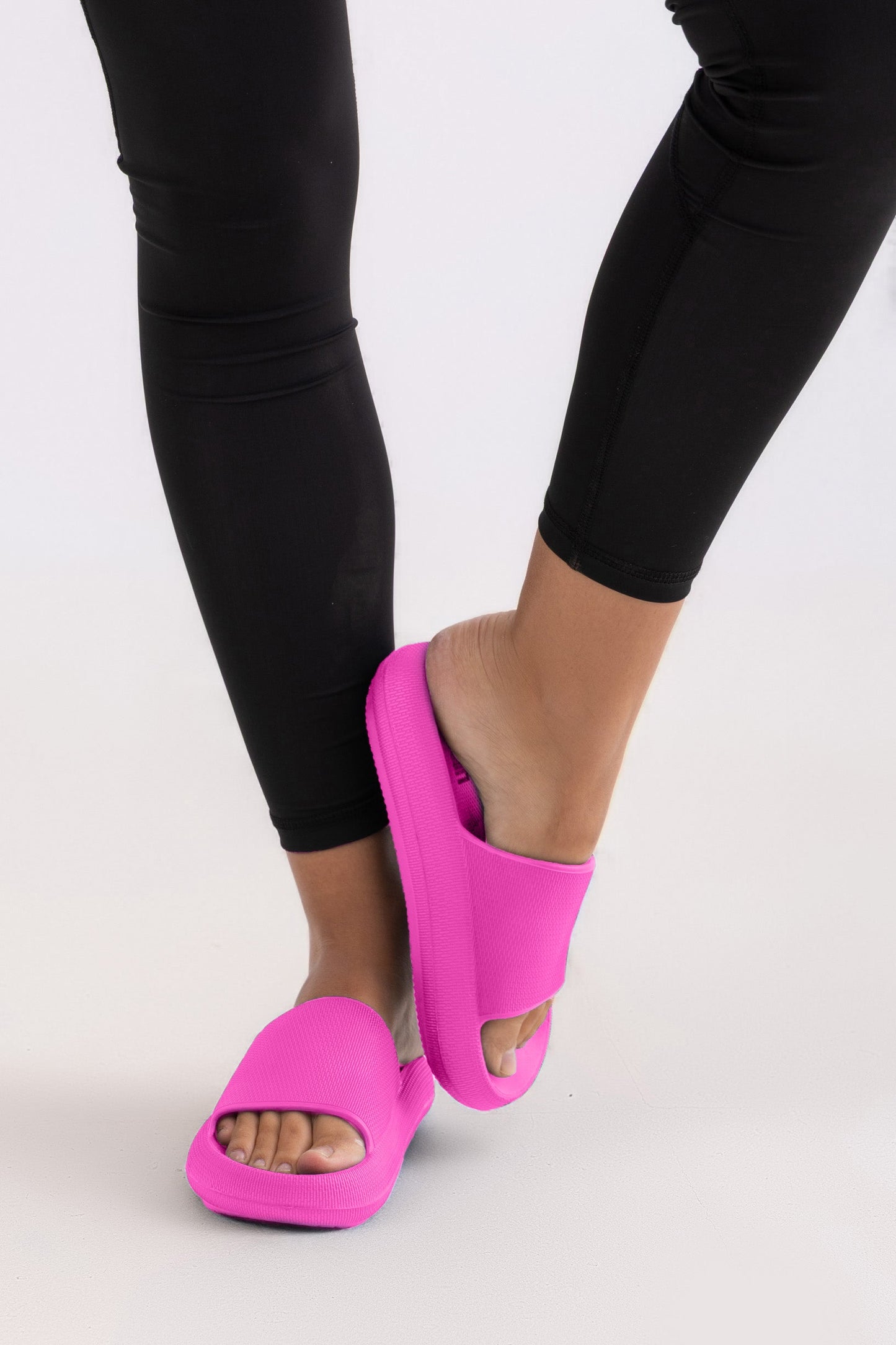 Person wearing bright pink slides with black leggings on a light gray background