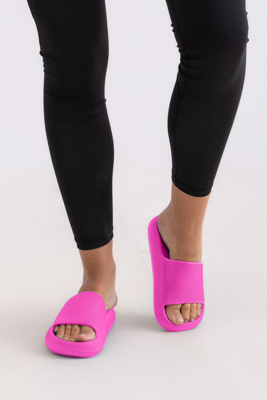 Person wearing bright pink sandals and black leggings on a white background